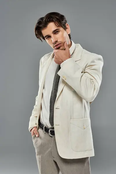 Un giovane vestito elegantemente si erge di fronte a uno sfondo grigio, mostrando la sua posa sicura e lo stile. — Stock Photo