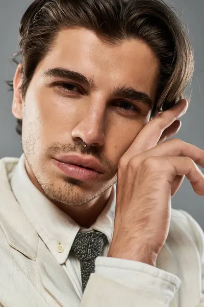 A stylish young man stands confidently in formal wear, showcasing a modern look against a grey setting. — Stock Photo