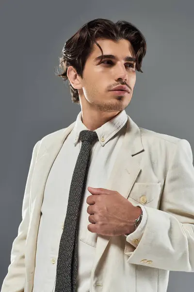 A young man in formal attire strikes a confident pose against a grey backdrop, radiating charm and sophistication. — Stock Photo