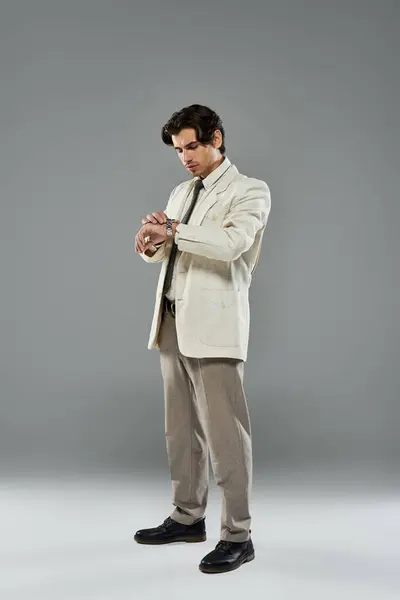 A young, handsome man dressed in formal attire intently checks his wristwatch while posing in a studio. — Stock Photo