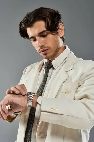 A handsome young man in elegant formal wear glances at his watch, exuding sophistication in a studio. — Stock Photo