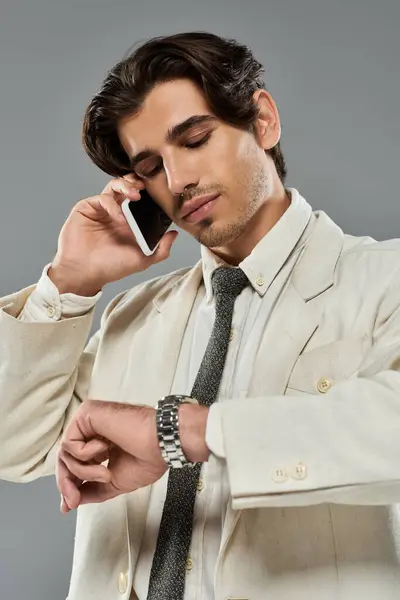 Un giovanotto in abito elegante fa una telefonata guardando il suo orologio in uno studio elegante. — Foto stock