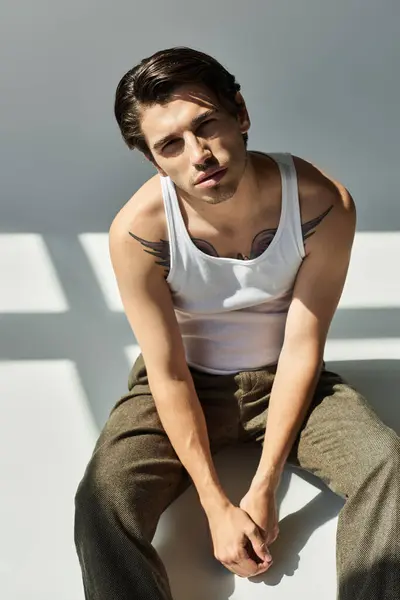 This young man, wearing a tank top, showcases his tattoo and exudes charisma in a minimalistic setting. — Stock Photo
