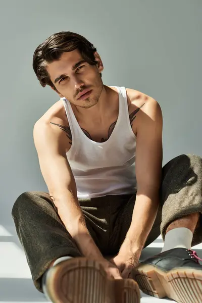 A young man with a striking tattoo sports a tank top, exuding confidence while seated against grey. — Stock Photo