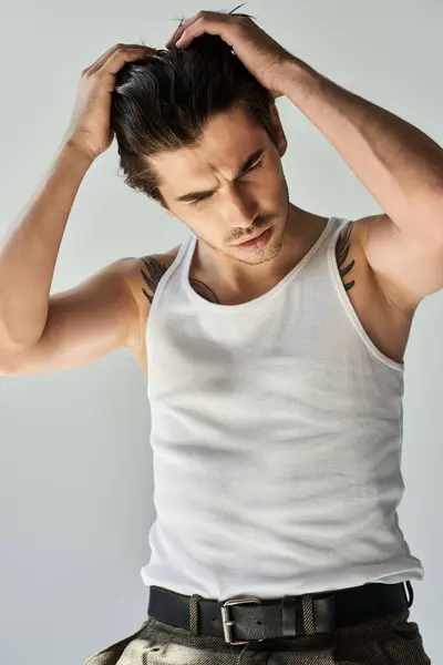 A young man in a tank top showcases his tattoos while deep in thought, illuminated by soft light. — Stock Photo