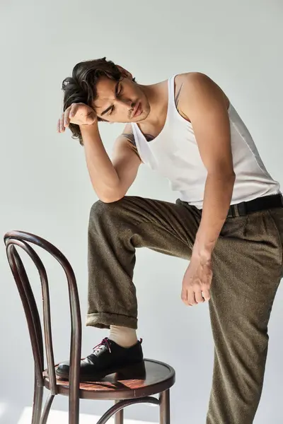 A handsome young man with a tattoo leans thoughtfully on a chair, showcasing his casual style and attitude. — Stock Photo