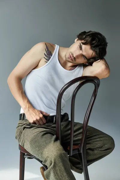 A handsome young man in a tank top relaxes in a minimalist setting, showing off his tattoo. — Stock Photo
