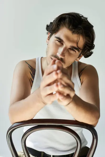 Ein junger Mann mit einer faszinierenden Tätowierung lehnt sich nach vorne und strahlt Zuversicht aus, während er ein lässiges Tank-Top trägt. — Stockfoto