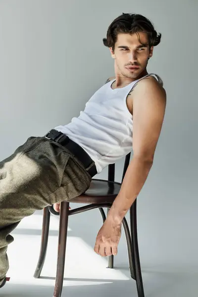 A young, handsome man showcases his tattoos while lounging effortlessly on a chair, dressed in casual attire. — Stock Photo