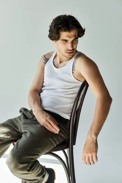 A confident young man in a tank top showcases his tattoos while sitting elegantly on a chair. — Stock Photo
