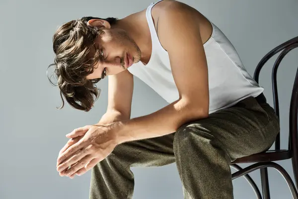 The young man with tousled hair and a tattoo softly contemplates life while sitting on a chair, dressed simply. — Stock Photo