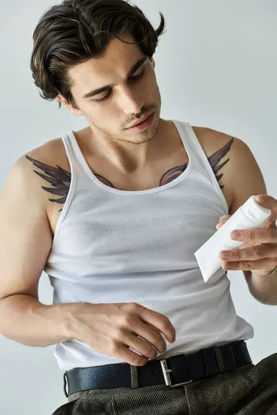 A handsome young man applies cream to his skin while sitting, showcasing his tattoos and relaxed demeanor. — Stock Photo