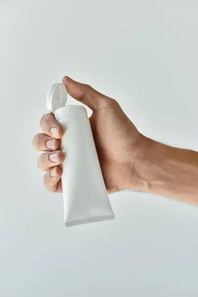 A young man holding beauty product in hand on a grey background. — Stock Photo