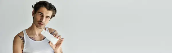 A handsome young man showcases his tattoos and beauty product while relaxing in a tank top, exuding a stylish, modern vibe. — Stock Photo
