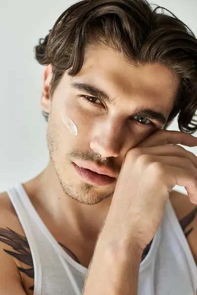 A stylish young man with tattoos delicately applies skincare while showcasing his confident expression. — Stock Photo