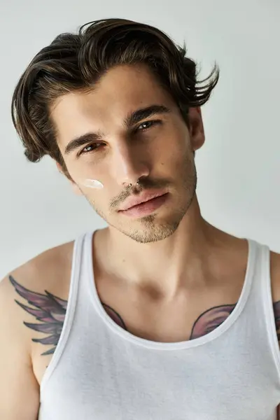 A confident young man showcases his tattoos while wearing a tank top, exuding charisma against a grey backdrop. — Stock Photo