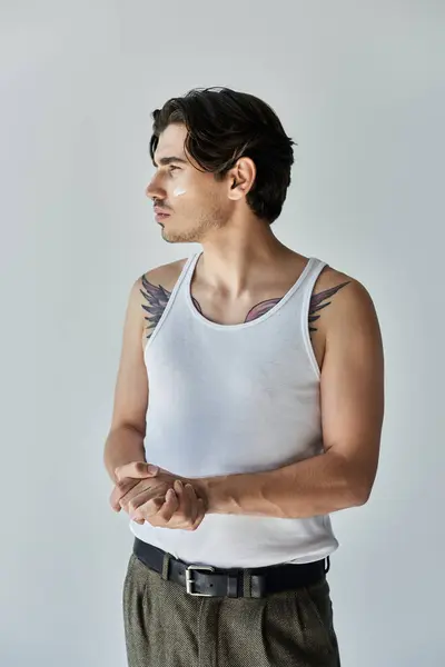 This striking young man stands confidently, displaying his tattoos in a casual tank top on a grey backdrop. — Stock Photo