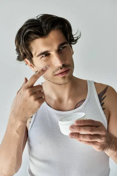This young man confidently applies skincare, blending modern style with a touch of personal art in a chill atmosphere. — Stock Photo