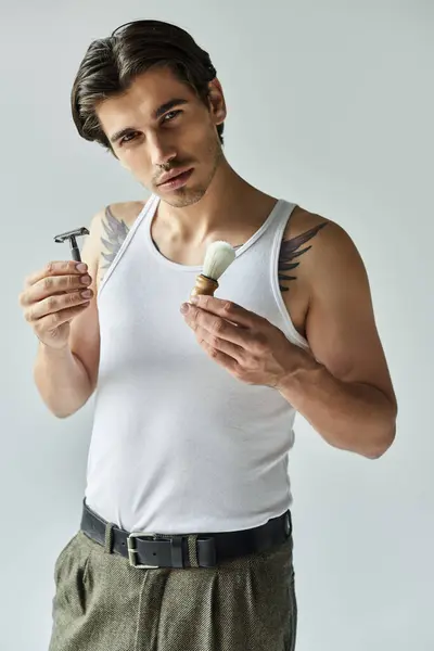 A confident young man in a tank top showcases grooming tools, exuding style and charm in a minimal setting. — Stock Photo