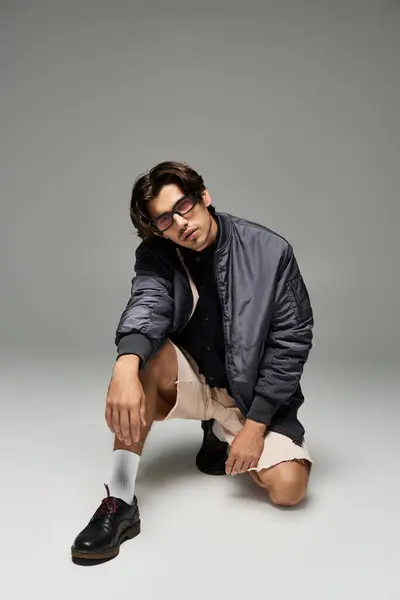 A stylish young man kneels, confidently displaying his fashionable autumn ensemble in a contemporary space. — Stock Photo