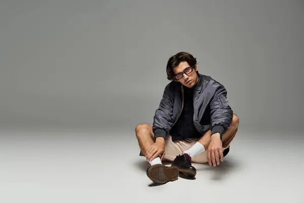 A young man confidently flaunts a fashionable autumn look while posing creatively in a minimalist space. — Stock Photo