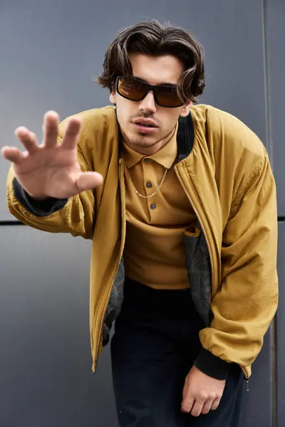 A stylish young man confidently poses in a trendy autumn outfit against an urban backdrop, exuding charisma. — Stock Photo