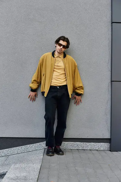 A fashionable young man stands against a contemporary wall, showcasing his autumn style with flair. — Stock Photo