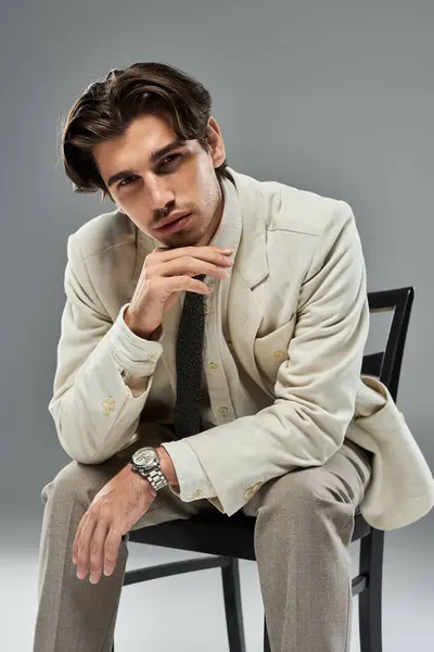Um homem jovem e bonito exibe seu elegante desgaste formal enquanto golpeia uma pose pensativa contra um pano de fundo cinza. — Fotografia de Stock
