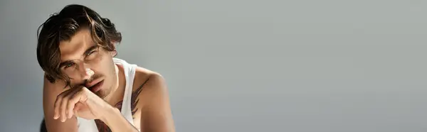 A striking young man showcases his tattoo while casually leaning, exuding confidence and charm. — Stock Photo