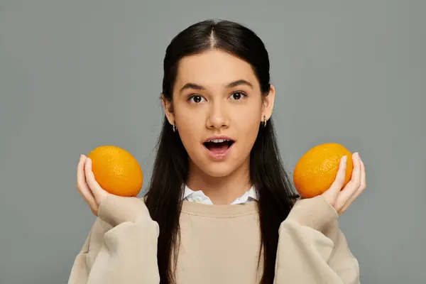A young woman showcases her emotions, holding two vibrant oranges with style. — Stock Photo