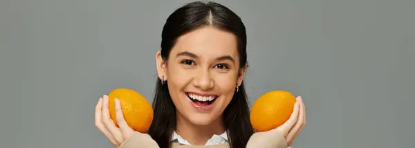 A happy, young woman expresses excitement while holding fresh oranges, dressed in trendy attire. — Stock Photo