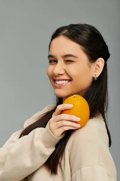 A stylish young woman beams with happiness, holding an orange close to her cheek. — Stock Photo