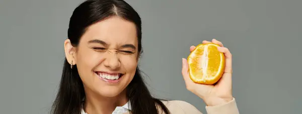 A cheerful young woman delights in a vibrant orange slice, flaunting her stylish look. — Stock Photo