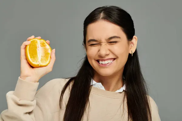 A stylish young woman radiates happiness while holding a vibrant orange slice. — Stock Photo