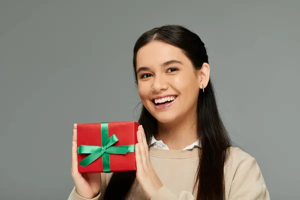 An excited young woman in fashionable clothing showcases a beautifully wrapped present with joy. — Stock Photo