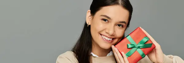 A pretty young woman in fashionable clothing beams with excitement while holding a festive gift. — Stock Photo