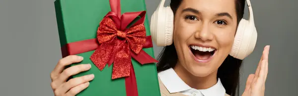 A young woman smiles excitedly, holding a beautifully wrapped gift full of holiday cheer. — Stock Photo