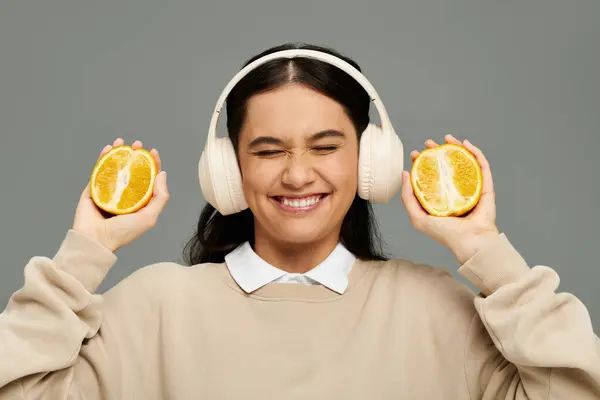 A young woman smiles brightly while playfully holding fresh oranges near her ears. — Stock Photo