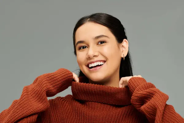 Una joven sonríe cálidamente mientras ajusta su elegante suéter, mostrando su vibrante personalidad. - foto de stock