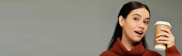Молодая женщина, одетая в модный и уютный наряд, наслаждается кофе с радостным выражением лица. — стоковое фото
