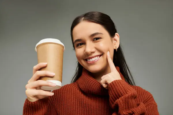 A young woman with a warm smile holds a coffee cup, radiating joy and style in a cozy setting. — Stock Photo