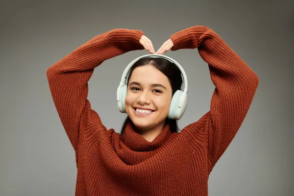 Una mujer joven en un suéter de moda forma alegremente un corazón con sus manos. - foto de stock