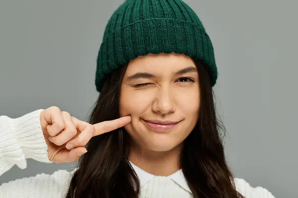 A young woman in fashionable clothing playfully winks while touching her cheek. — Stock Photo