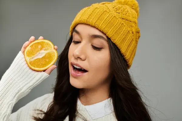 A young woman with a vibrant hat joyfully holds up a citrus slice, radiating happiness. — Foto stock