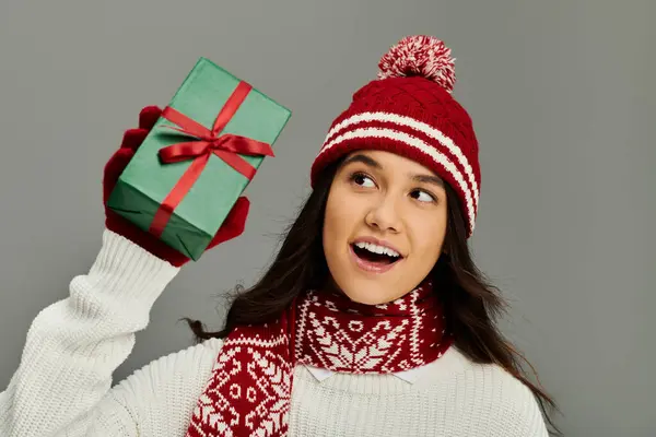 A young woman shows her excitement while holding a beautifully wrapped gift, dressed warmly. — Stock Photo
