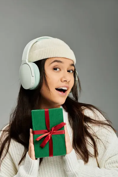 A pretty young woman smiles brightly as she poses with a wrapped gift, full of excitement. — Stock Photo