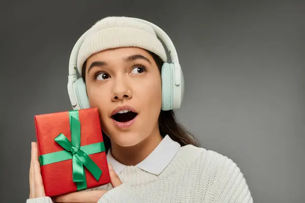 Fröhliche junge Frau in trendiger Kleidung bringt Überraschung mit einem Geschenk zum Ausdruck und verkörpert festliche Begeisterung. — Stockfoto