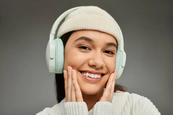 A young woman in a stylish winter outfit smiles while enjoying music, creating warmth. — Stock Photo