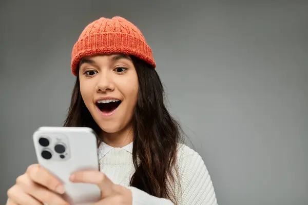 A young woman excitedly interacts with her smartphone, showing off her stylish outfit. — Stock Photo