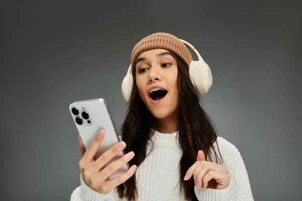 A young woman wearing a stylish outfit and headphones expresses excitement while using her phone. — Stock Photo